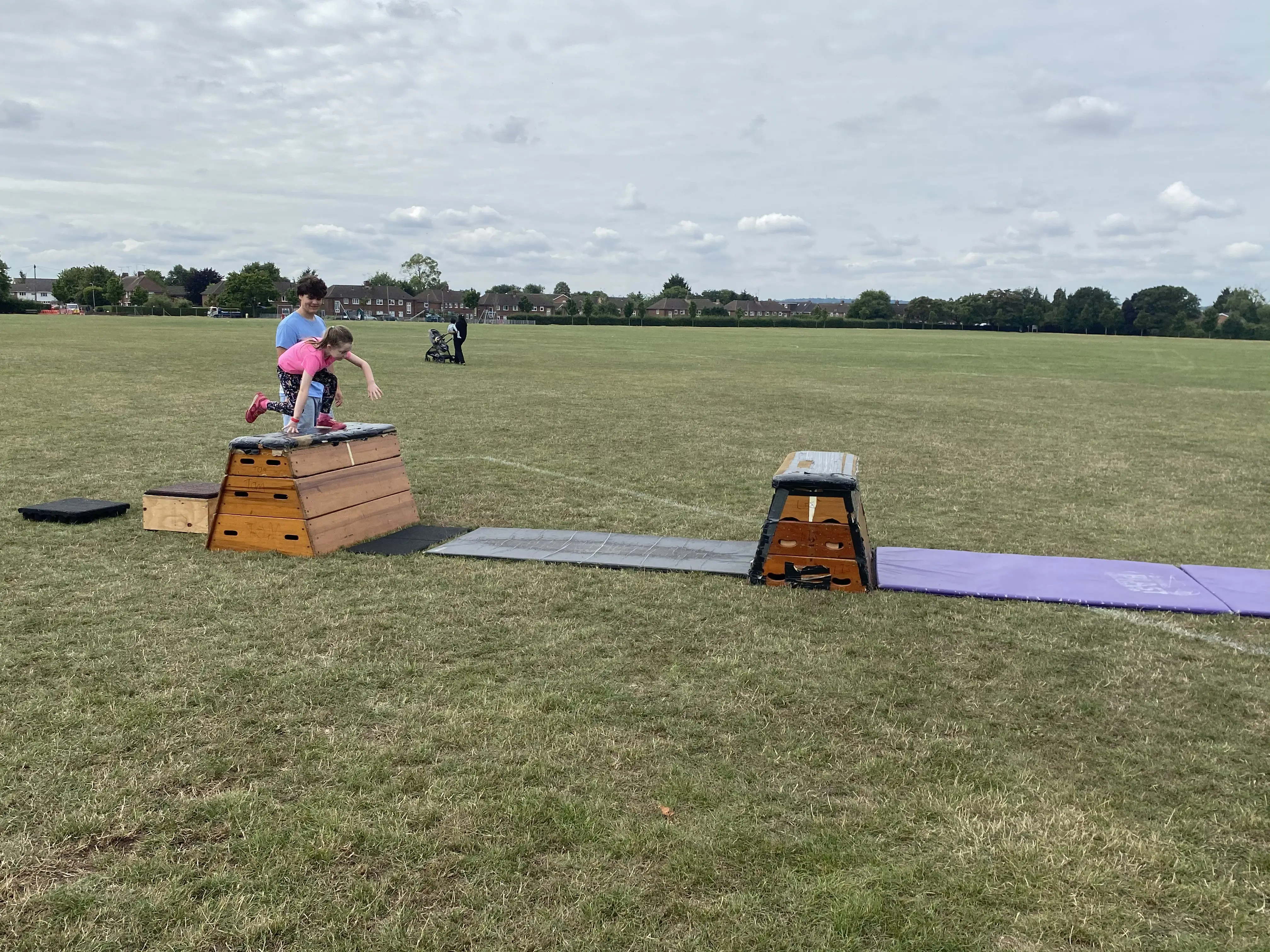 Girl jumping over old fashioned gym vaulting equipment set out in a large field