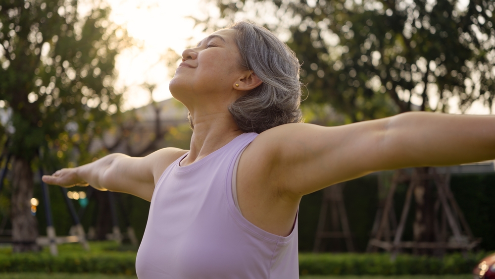 Woman standing outside with eyes closed and arms outstretched
