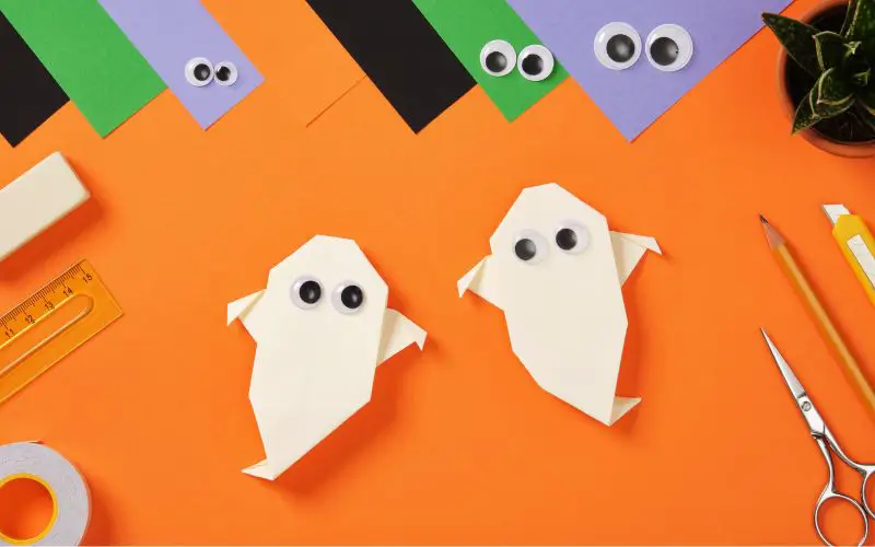 Origami ghosts surrounded by craft supplies and orange paper.
