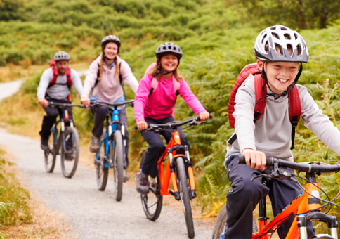 Boy, girl, woman and man in a line cycling along countryside trail