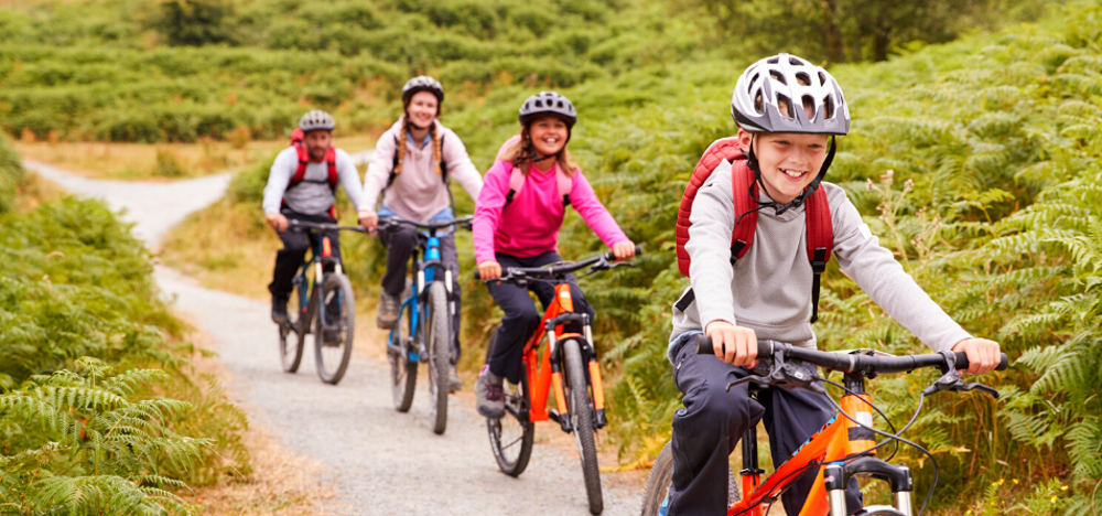 Boy, girl, woman and man in a line cycling along countryside trail