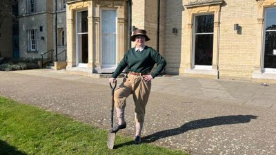 Visitor Host, Rachel, dressed as a Land Girl stood outside Chelmsford Museum with her foot on a spade. 
