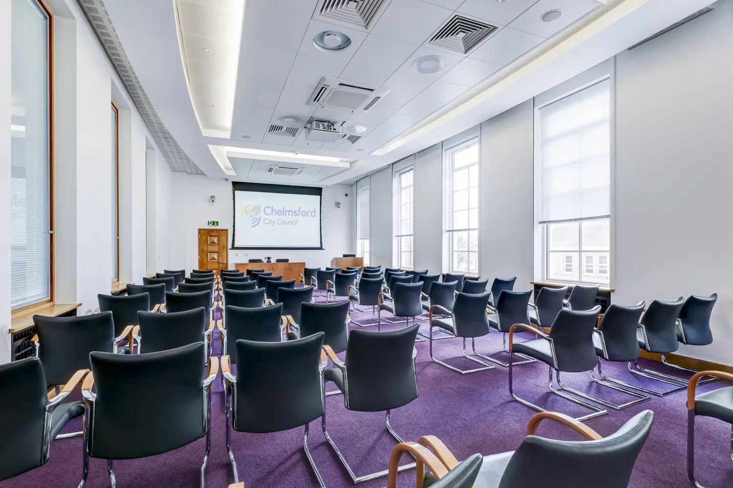 Meeting room set out with audience-style seating, facing large screen