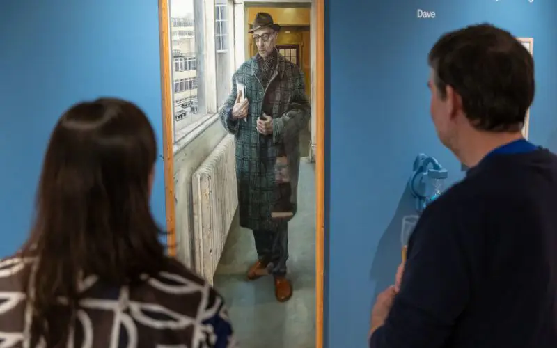 A man a woman facing away from the camera look at a portrait of a man.