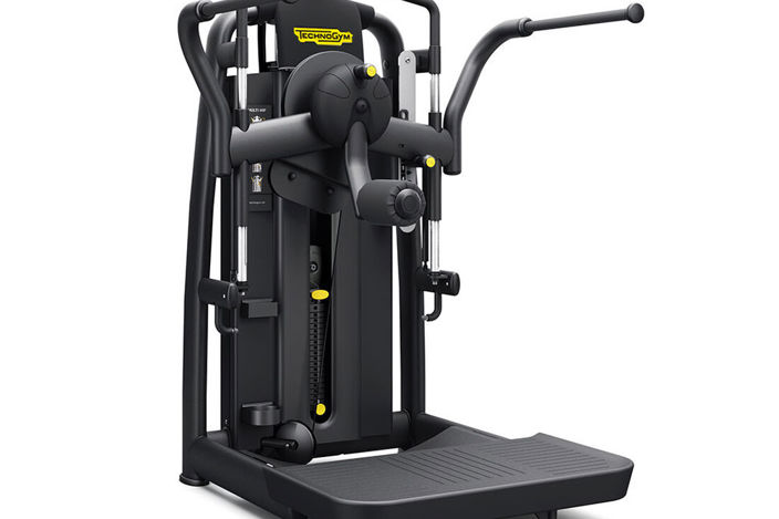A piece of Technogym equipment with a standing platform, two shoulder-high handles, and a padded lever with circular rotation. There is also a screen for tracking progress.