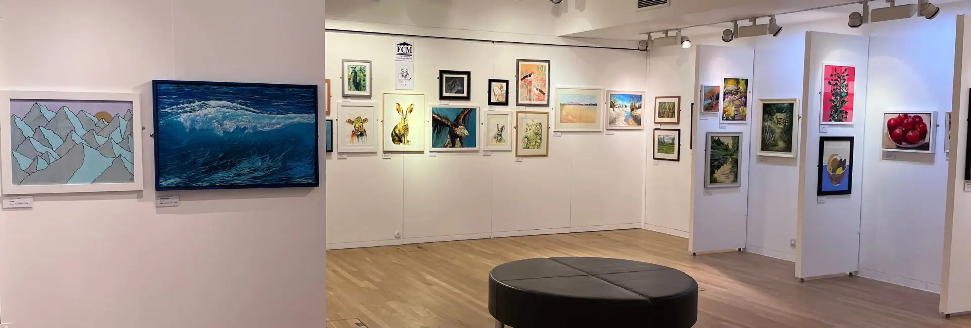 Paintings by various artists on display in the temporary exhibition space. A seating area is in the middle of the room. 