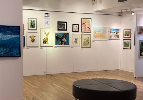 Paintings by various artists on display in the temporary exhibition space. A seating area is in the middle of the room. 