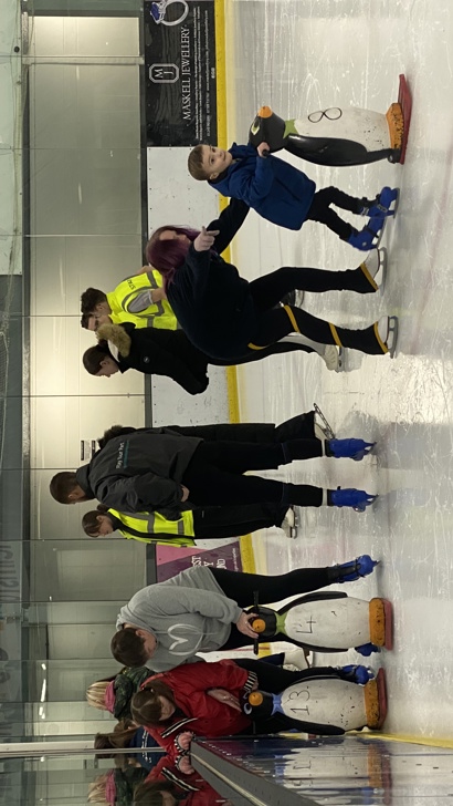 Group of young children learning to ice skate with penguin aids