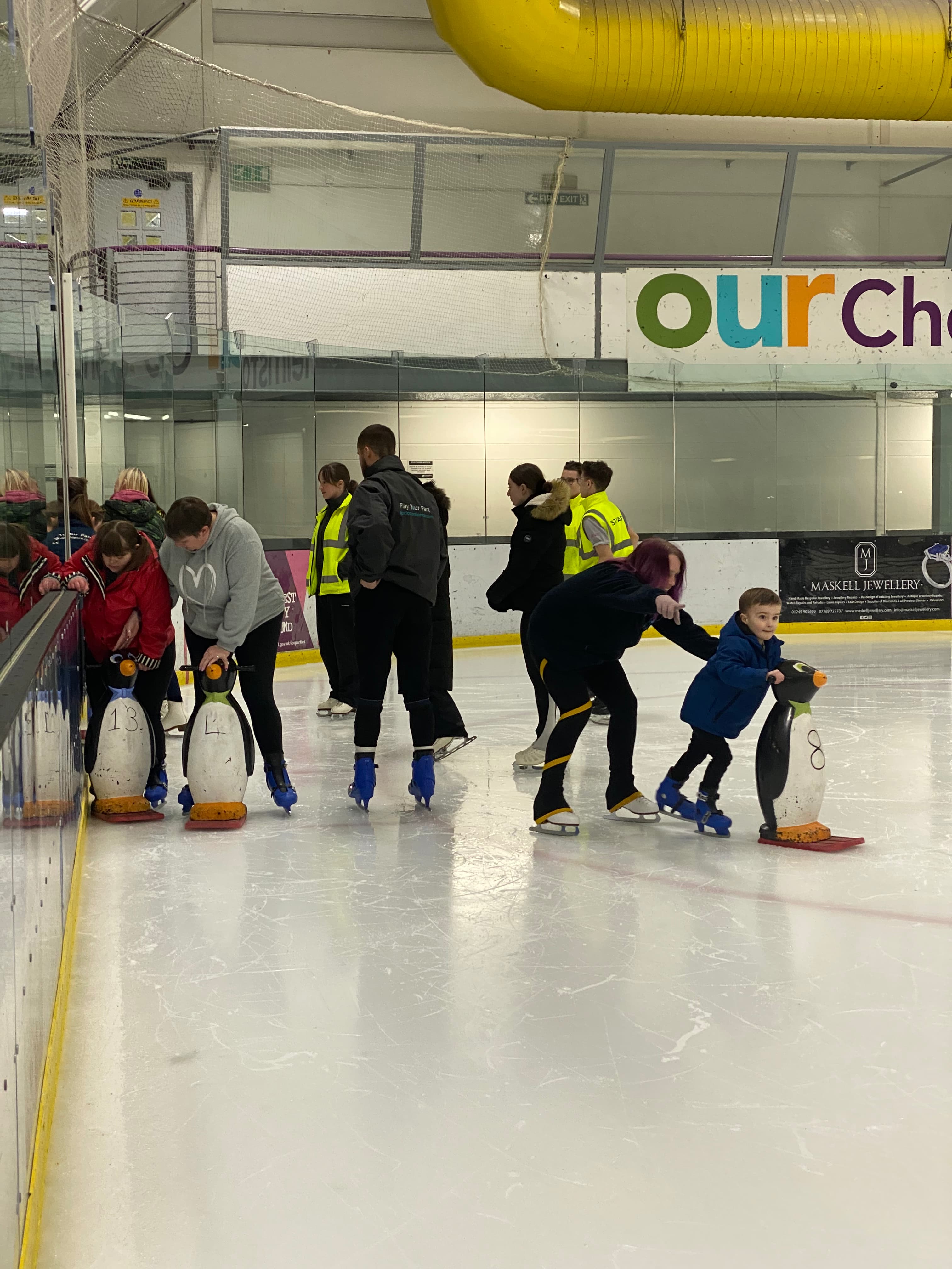 Group of young children learning to ice skate with penguin aids