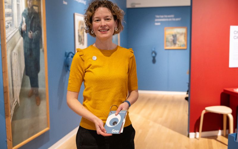 A woman with a bright yellow shirt standing in the Shifting Perspectives exhibition.