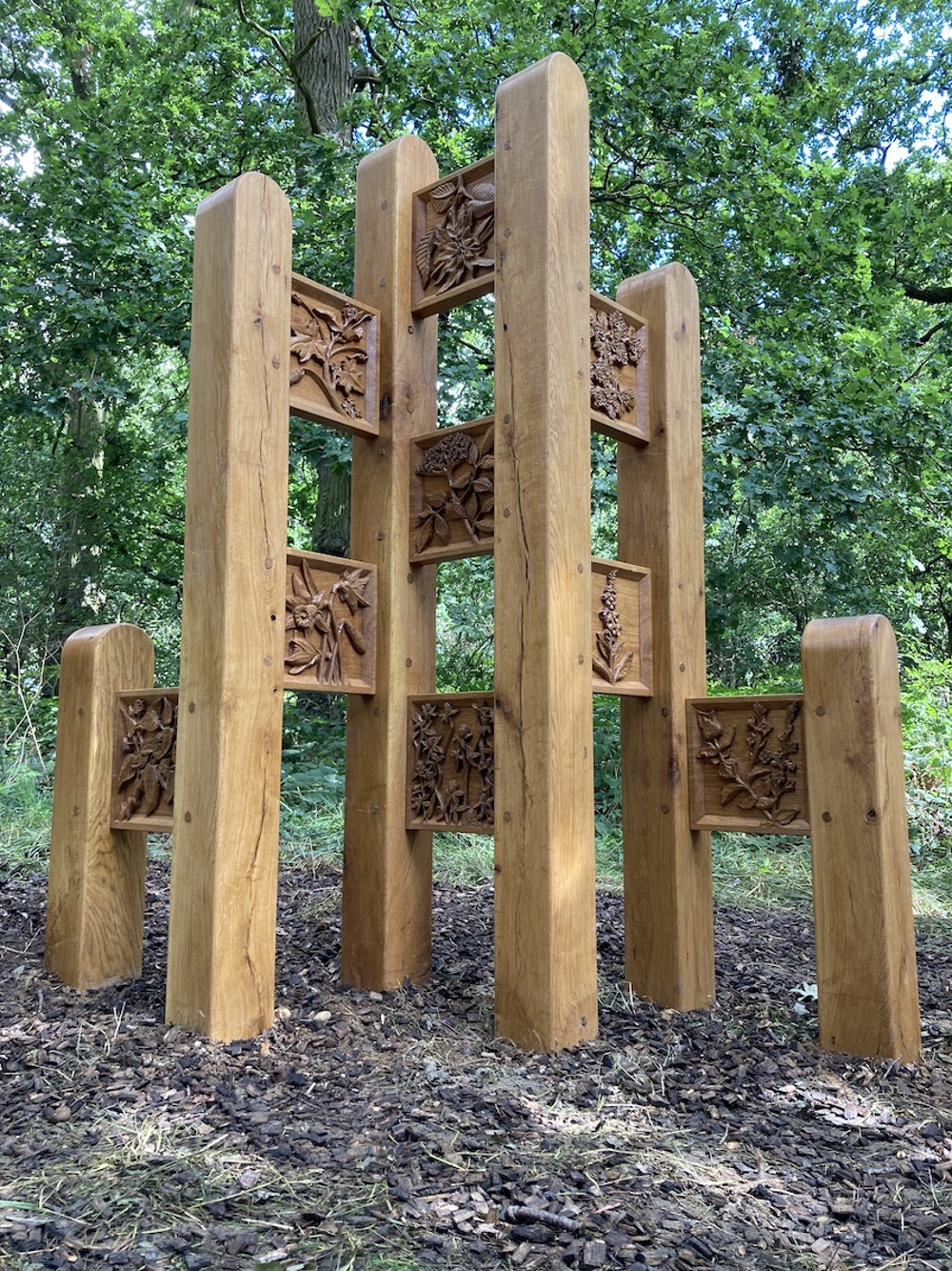 Large oak sculpture featuring tall posts and carved square panels featuring reliefs of flowers and other flora