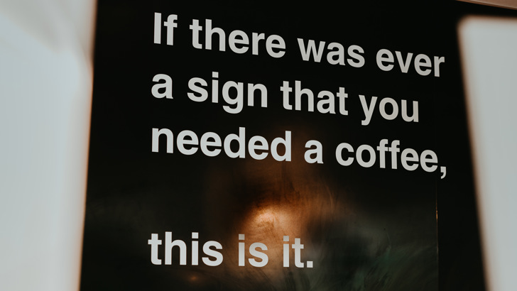 Large black sign, featuring the slogan "If ever there was a sign you needed a coffee, this is it."