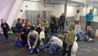 Group of adults and children sat on benches putting on blue ice skates at an indoor ice rink preview