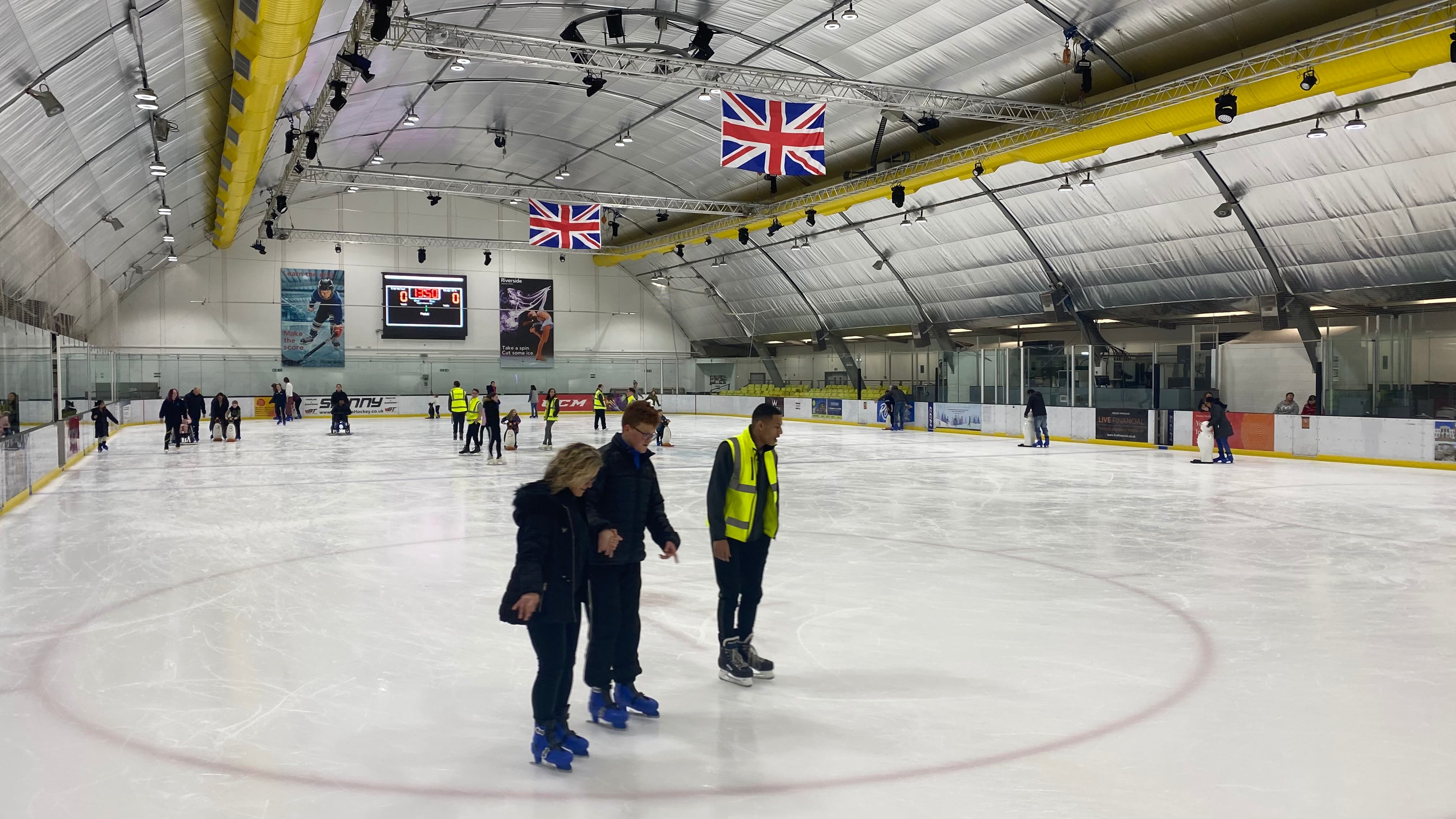 People in high visibility jackets helping others to learn how to ice skate