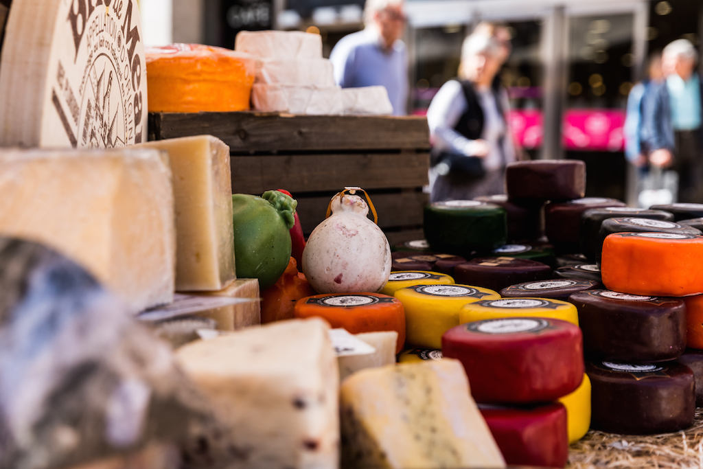 People looking at various cheeses laid out on a market stall