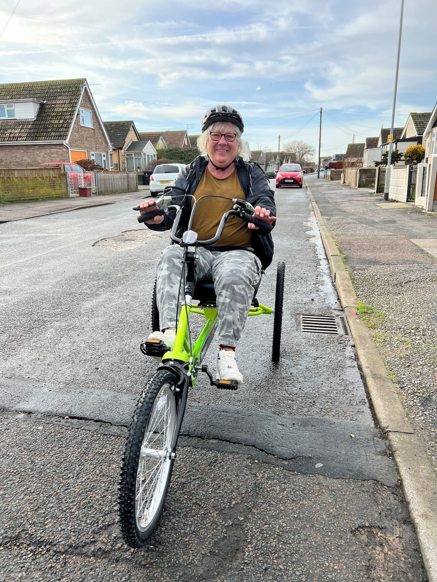 Smiling older lady on a green three-wheeled bike on a residential street