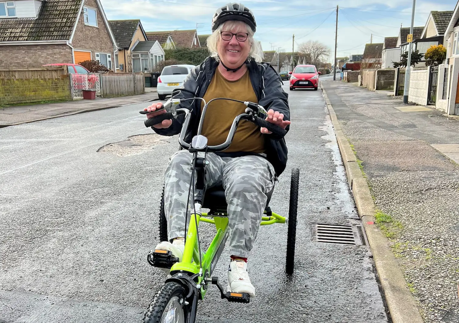 Smiling older lady on a green three-wheeled bike on a residential street