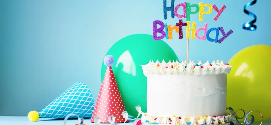 Cake featuring a 'Happy birthday' topper, surrounded by balloons, party hats and streamer