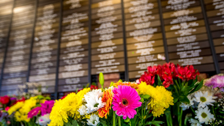 Colourful flowers in front of wall full of small plaques bearing the names of deceased loved ones
