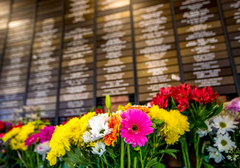 Colourful flowers in front of wall full of small plaques bearing the names of deceased loved ones