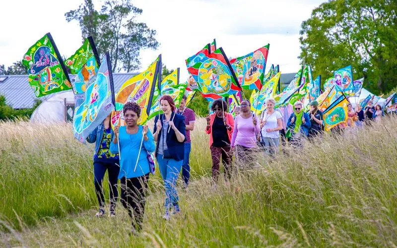 People carrying the colourful C100 flags through a field.
