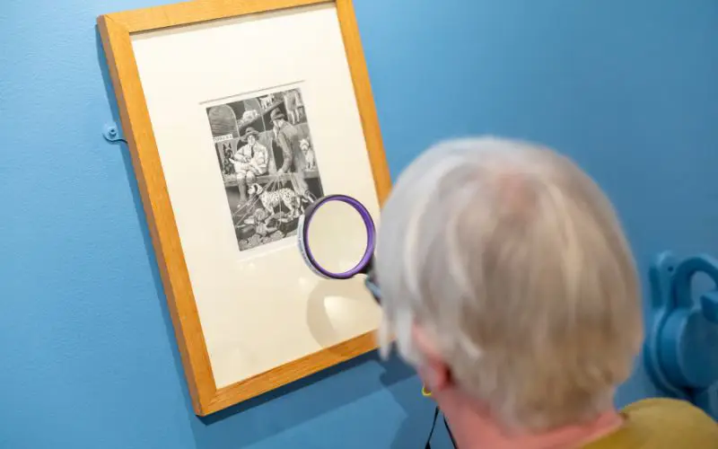 A woman looks closely at a piece of art with a magnifying glass.