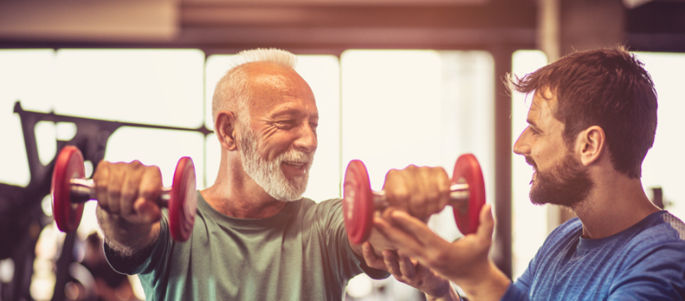 Personal trainer helping older man who is holding small dumbbells