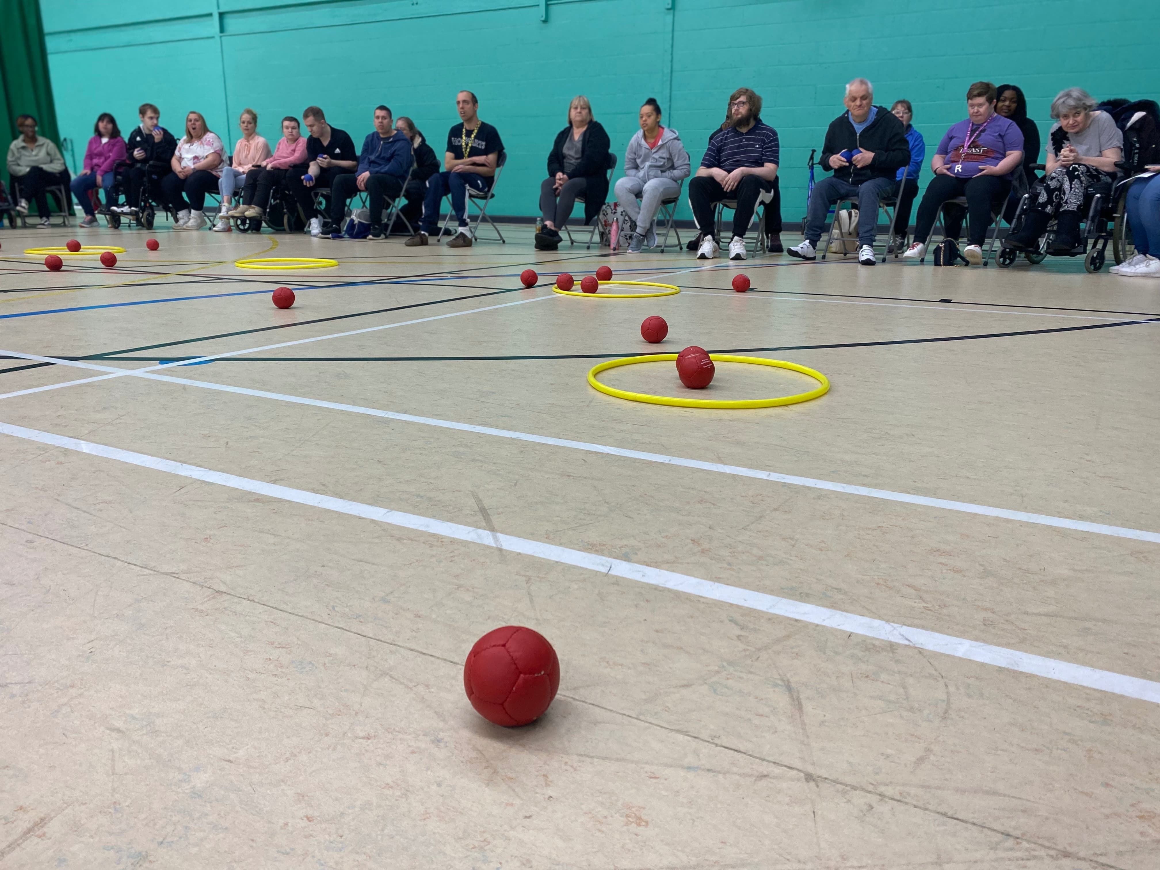 red Boccia balls on the floor of a sports hall next to a yellow hoop
