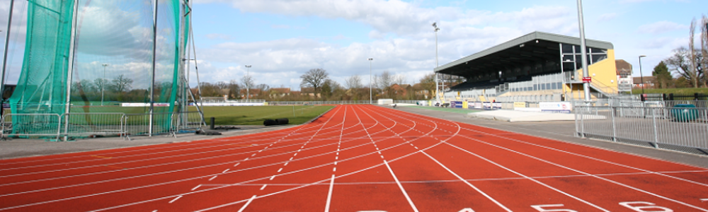 Athletics track at CSAC as seen from start line, with grandstand and throwing cage in the distance