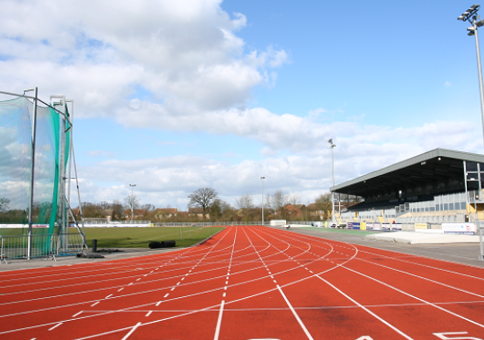 Athletics track at CSAC as seen from start line, with grandstand and throwing cage in the distance