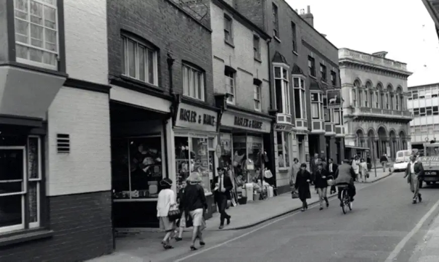 People walking past row of shops (black and white photo from 1958)
