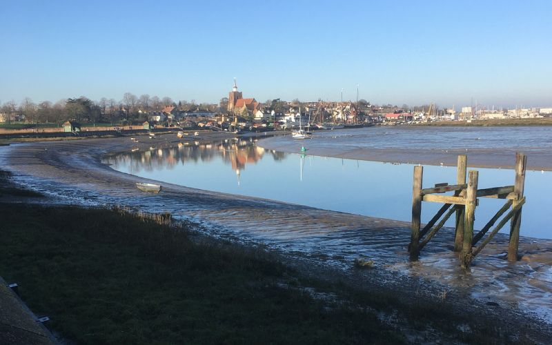 A seaside town where the coast is curved. Boats can be seen in the shallow water. 