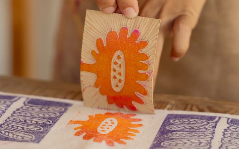A close up of someone creating a lino print with an orange flower. 