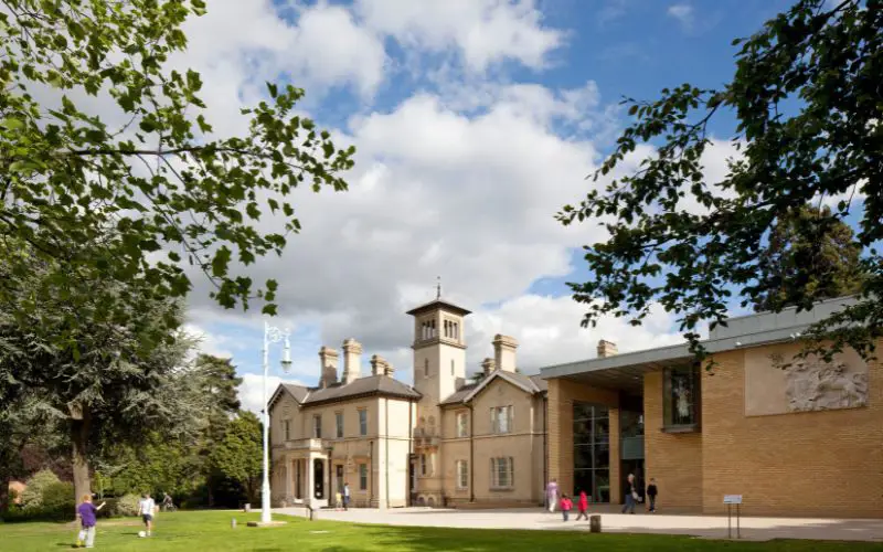 The exterior of Chelmsford Museum with visitors playing on the front lawn. 