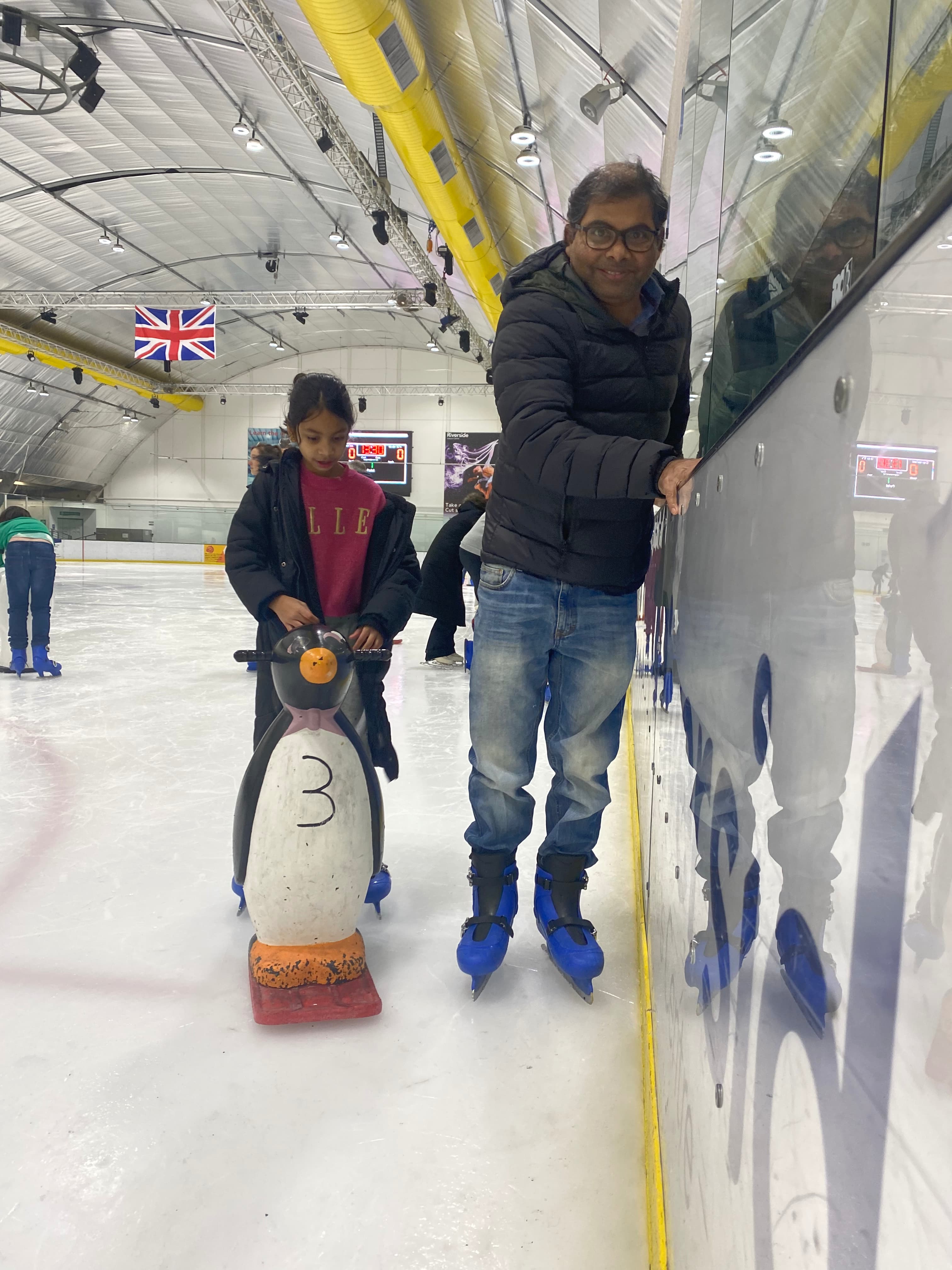 Father and daughter learning to ice skate, smiling.