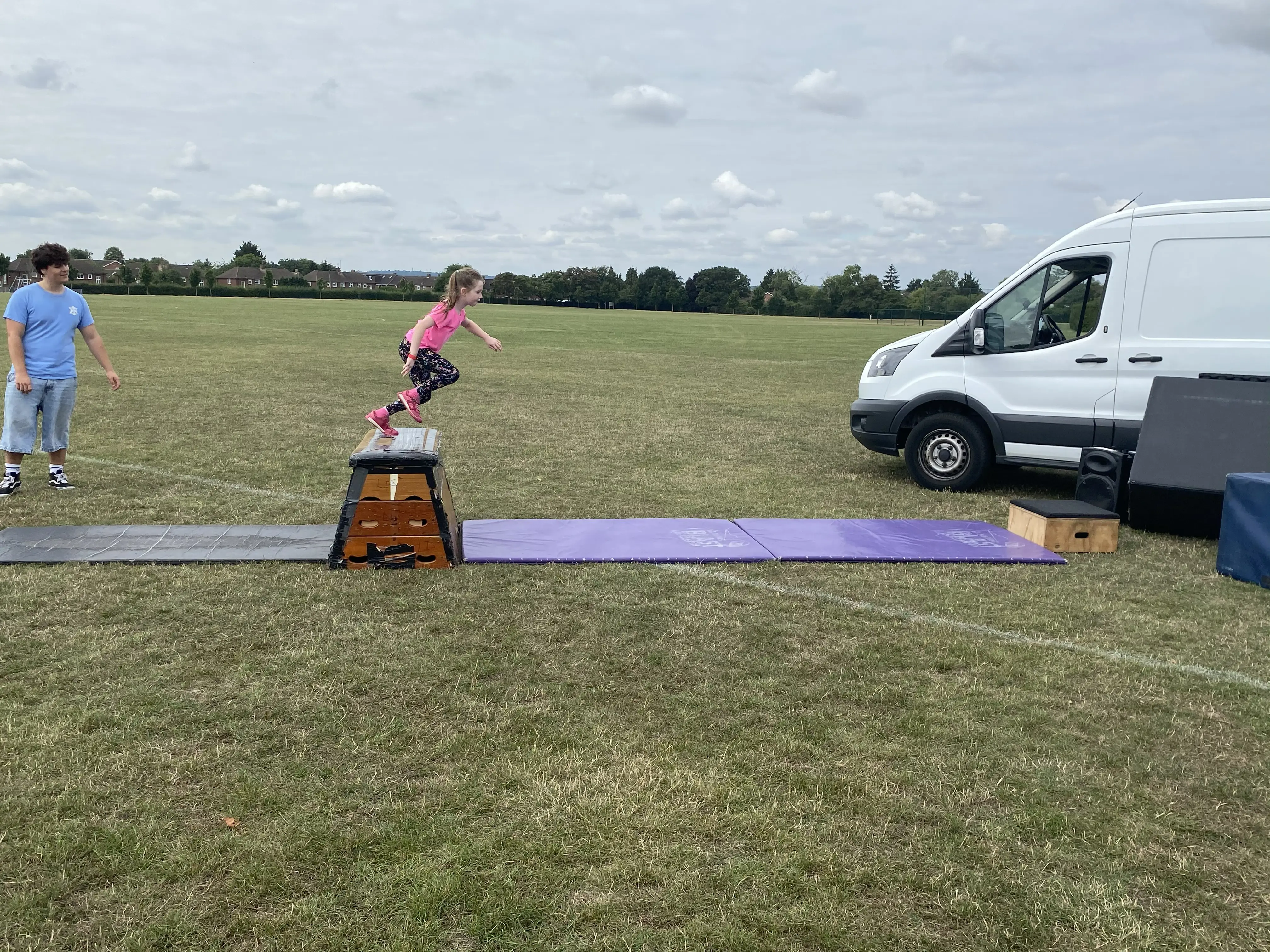 Girl jumping over old fashioned gym vaulting equipment set out in a large field