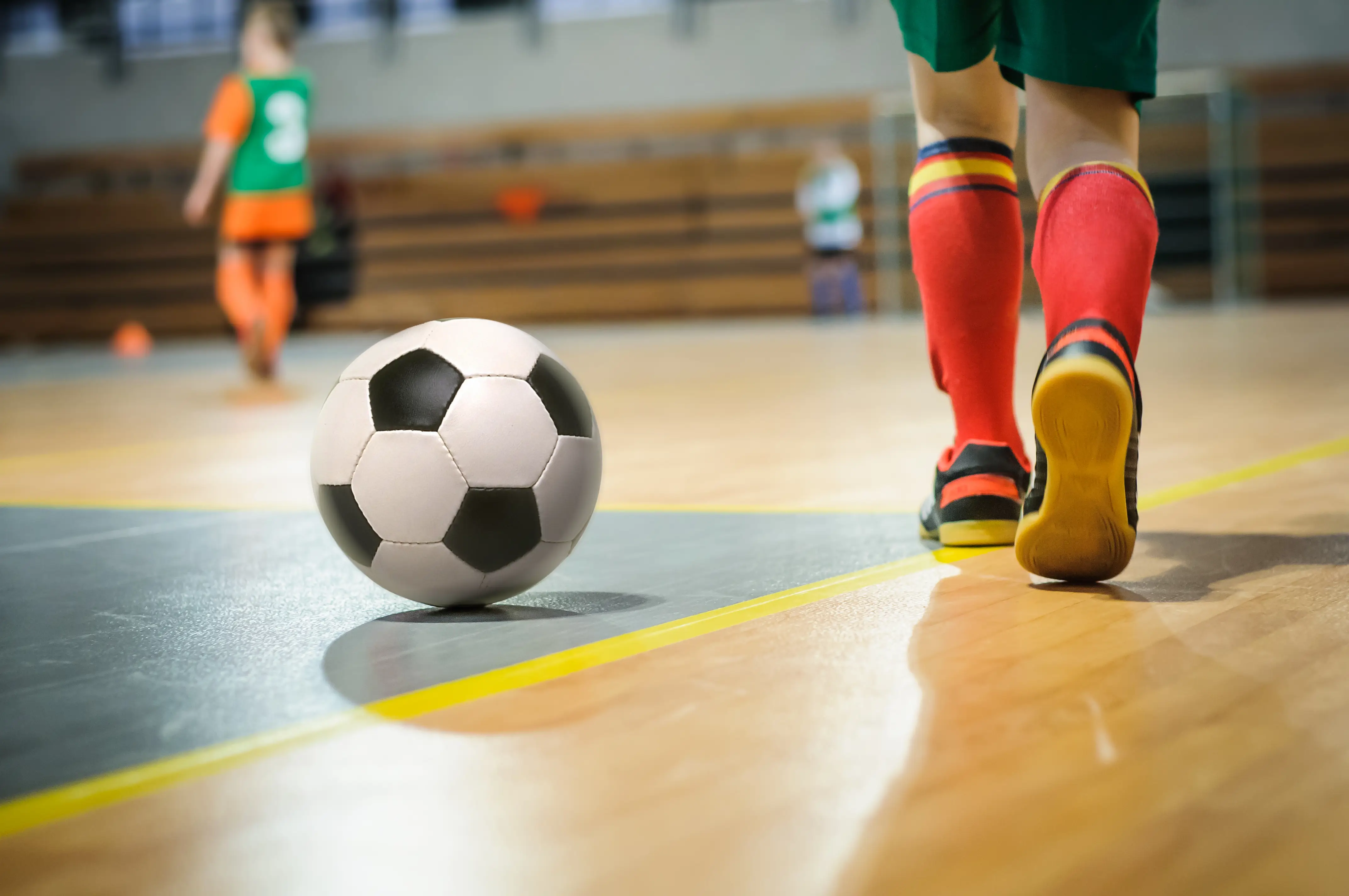 Young footballer in boots walking across a sports hall pitch