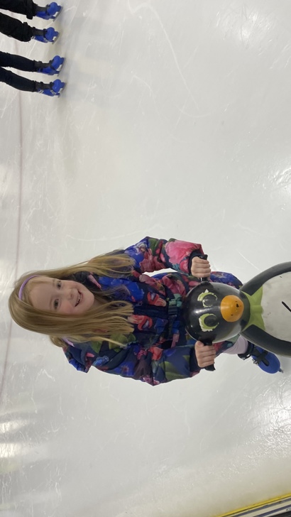 Young girl ice skating holding onto a plastic penguin aid for balance