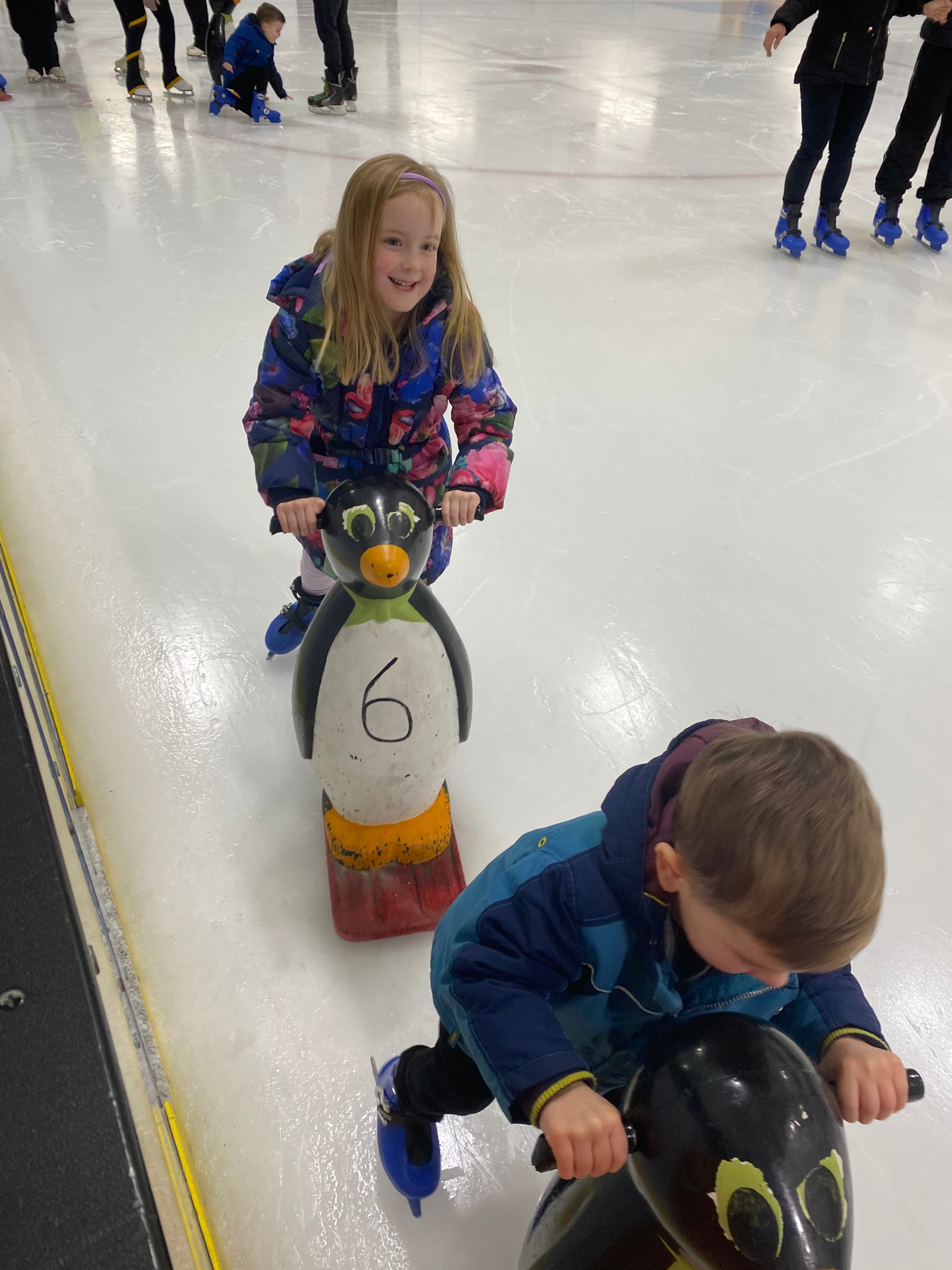 Young girl ice skating holding onto a plastic penguin aid for balance