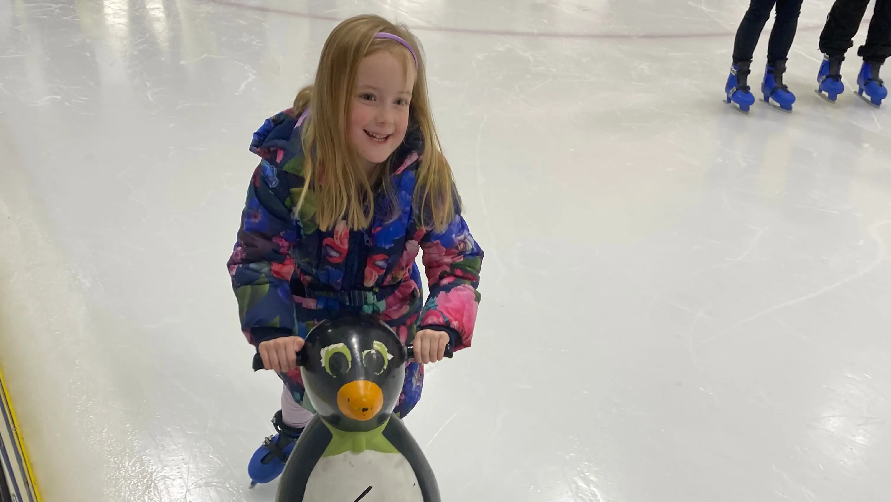 Young girl ice skating holding onto a plastic penguin aid for balance