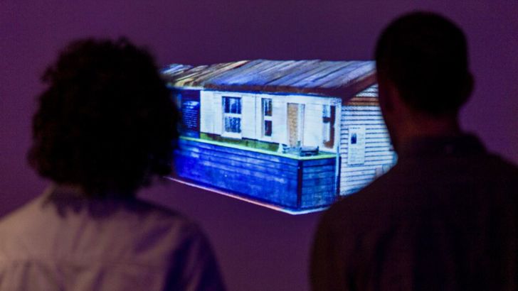 Two people standing in front of a screen with a projection of the scan of the Writtle Hut. 