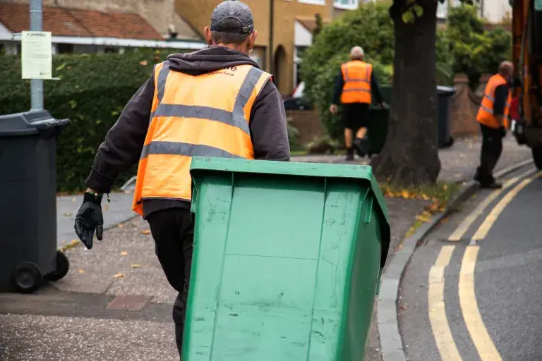 Man in an orange high vis pulling a green wheelie bin
