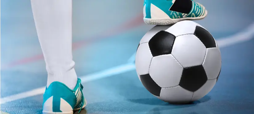 Person's foot rest on football on indoor pitch