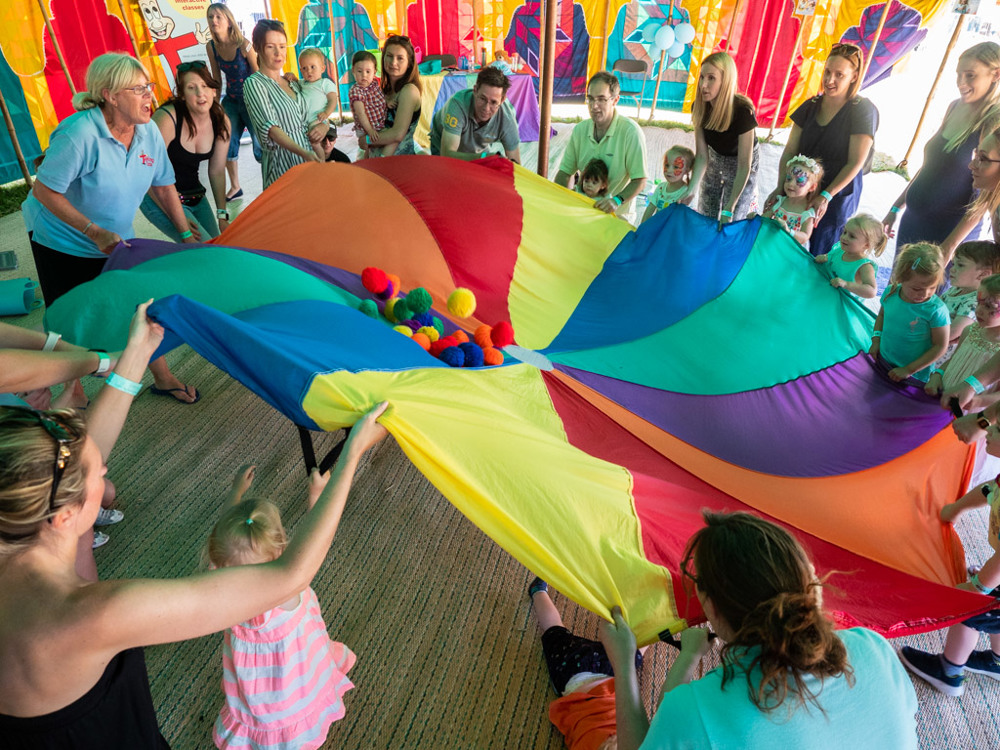 Large group of children playing with large, multi-coloured parachute