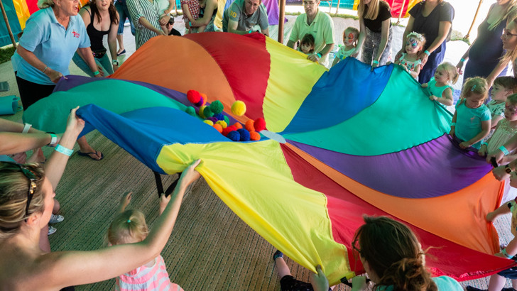 Large group of children playing with large, multi-coloured parachute