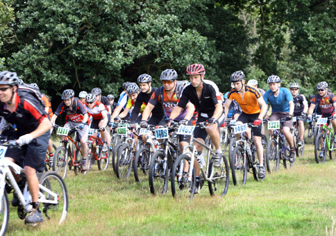 Large group of mountain bikers racing across grassy area