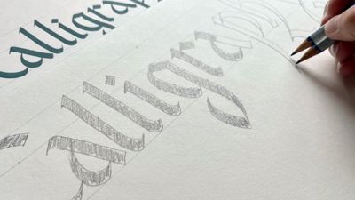 A person writing calligraphy with two pencils attached together. 