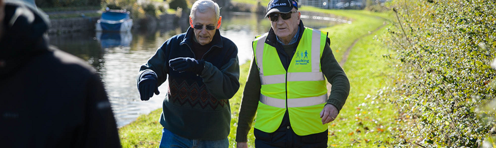 Two older gentlemen walking along grassy trail alongside river