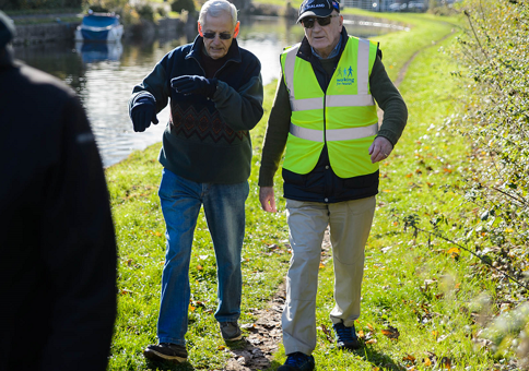 Two older gentlemen walking along grassy trail alongside river