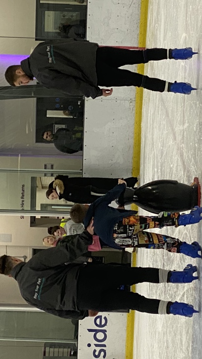 Young boy learning to ice skate, holding onto a penguin aid, with coaches either side.